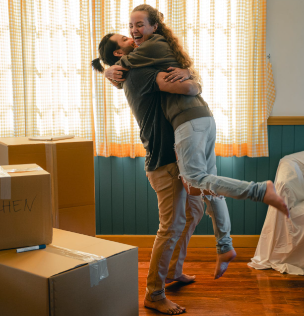 Happy homeowners holding each other with boxes on the floor