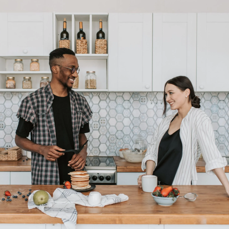 Couple smiling at each other in kitchen making pancakes with fruit